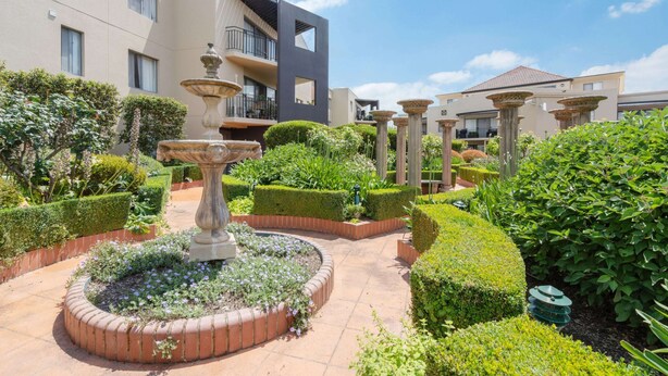 A courtyard with a central fountain, surrounded by well-manicured hedges and a variety of plants. - Sleek 2-bed Apartment in Vibrant Kingston (Canberra)