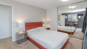 A modern bedroom with a large bed, two bedside tables with lamps, a mirror, and a carpeted floor. - Sleek 2-bed Apartment in Vibrant Kingston (Canberra)