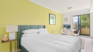 A hotel room with a bed, a bedside table with a lamp, a chair, and a view of the outdoors. - Serene Studio With Balcony in Prime Location (Sydney)