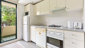 A compact kitchen with white appliances, a dishwasher, a stove, and a microwave. - Serene Studio With Balcony in Prime Location (Sydney)