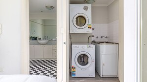 A compact laundry room with a washing machine and dryer, a sink, and a checkered floor. - Serene Studio With Balcony in Prime Location (Sydney)