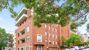 A multi-story brick building with balconies, a clear sky, and parked cars along the street. - Serene Studio With Balcony in Prime Location (Sydney)