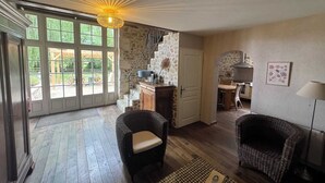 Amplia sala de estar con mobiliario de mimbre, una escalera que conduce a una cocina y ventanas grandes con vistas al exterior.