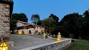 Un edificio de piedra con tejado de tejas, un patio empedrado y un muro de piedra con un farol.