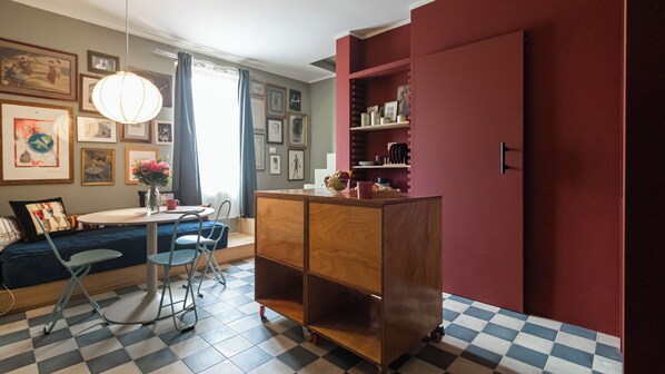 A room with a checkered floor, a wooden cabinet, a dining table with chairs, and a window with curtains. - Italianway Easy - Sarpi 58 (Milan)