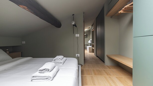 Une chambre d’hôtel moderne avec un grand lit, un banc en bois et un dressing.