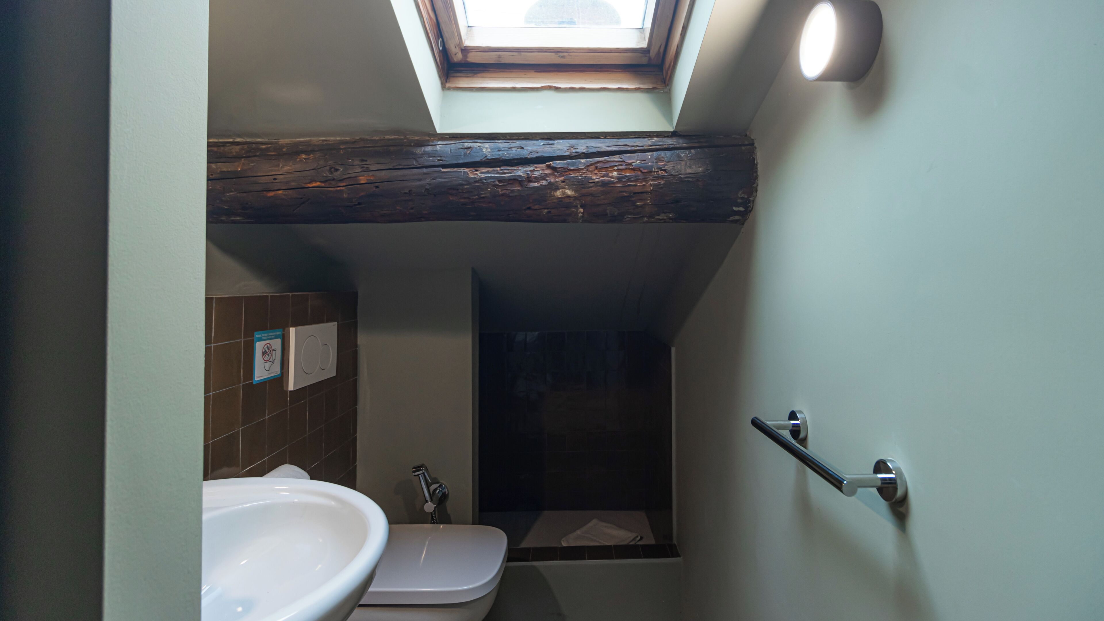 A bathroom with a skylight, a white sink, a toilet, and a shower.