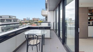 A modern apartment with a balcony, a glass door leading to a kitchen, and a city view. - Eclectic 1-bed Apartment With Pool and Gym (Melbourne)