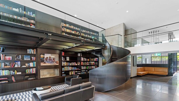 A modern library with bookshelves, a curved staircase, and a seating area. - Eclectic 1-bed Apartment With Pool and Gym (Melbourne)