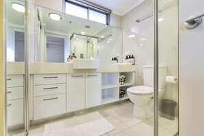 A modern bathroom with a large mirror, white cabinets, a toilet, and a glass shower enclosure. - Stylish 1-bed Darwin City Stay With Balcony Views (Darwin)