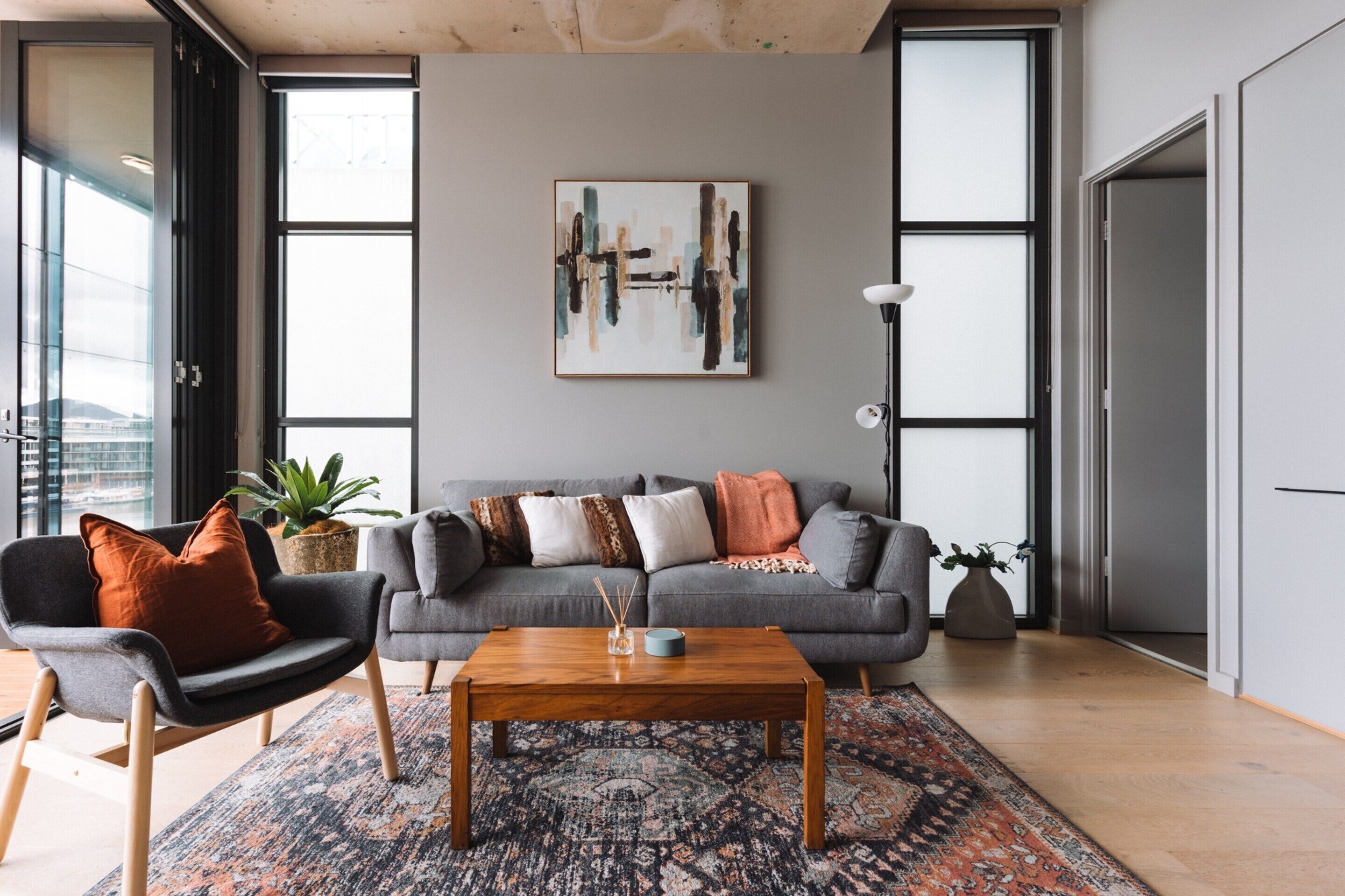 A modern living room with a grey sofa, a wooden coffee table, and a large abstract painting on the wall.