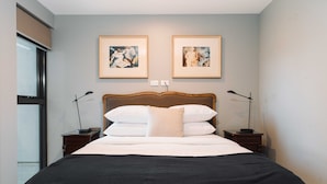 Uma cama bem arrumada com cabeceira de madeira, duas mesas de cabeceira com abajures e duas obras de arte emolduradas na parede.