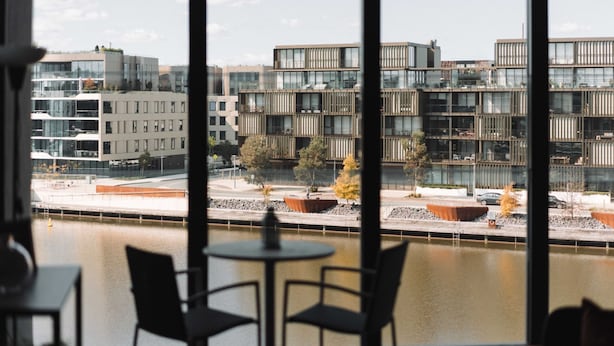 Um edifício moderno com vários andares e grandes janelas, visto de uma varanda com mesa e cadeiras.