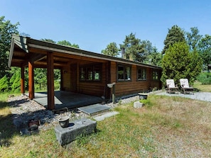 A wooden cabin with a covered porch, a small outdoor seating area, and a gravel path leading to the entrance.