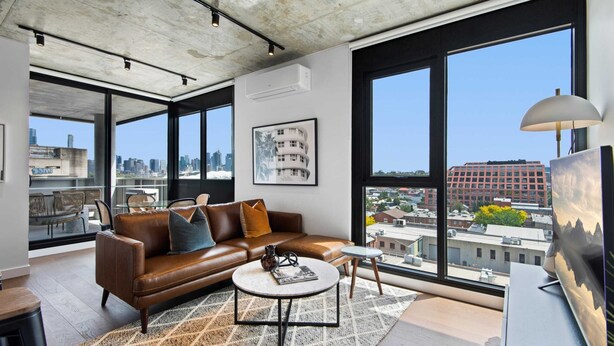 A modern living room with a leather sofa, a coffee table, and large windows offering a city view. - Executive 2-bed Apartment With Views, Gym and Spa (Melbourne)