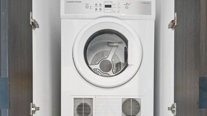 A stacked washer and dryer unit with a control panel, located in a room with a wooden door and a tiled floor. - Executive 2-bed Apartment With Views, Gym and Spa (Melbourne)