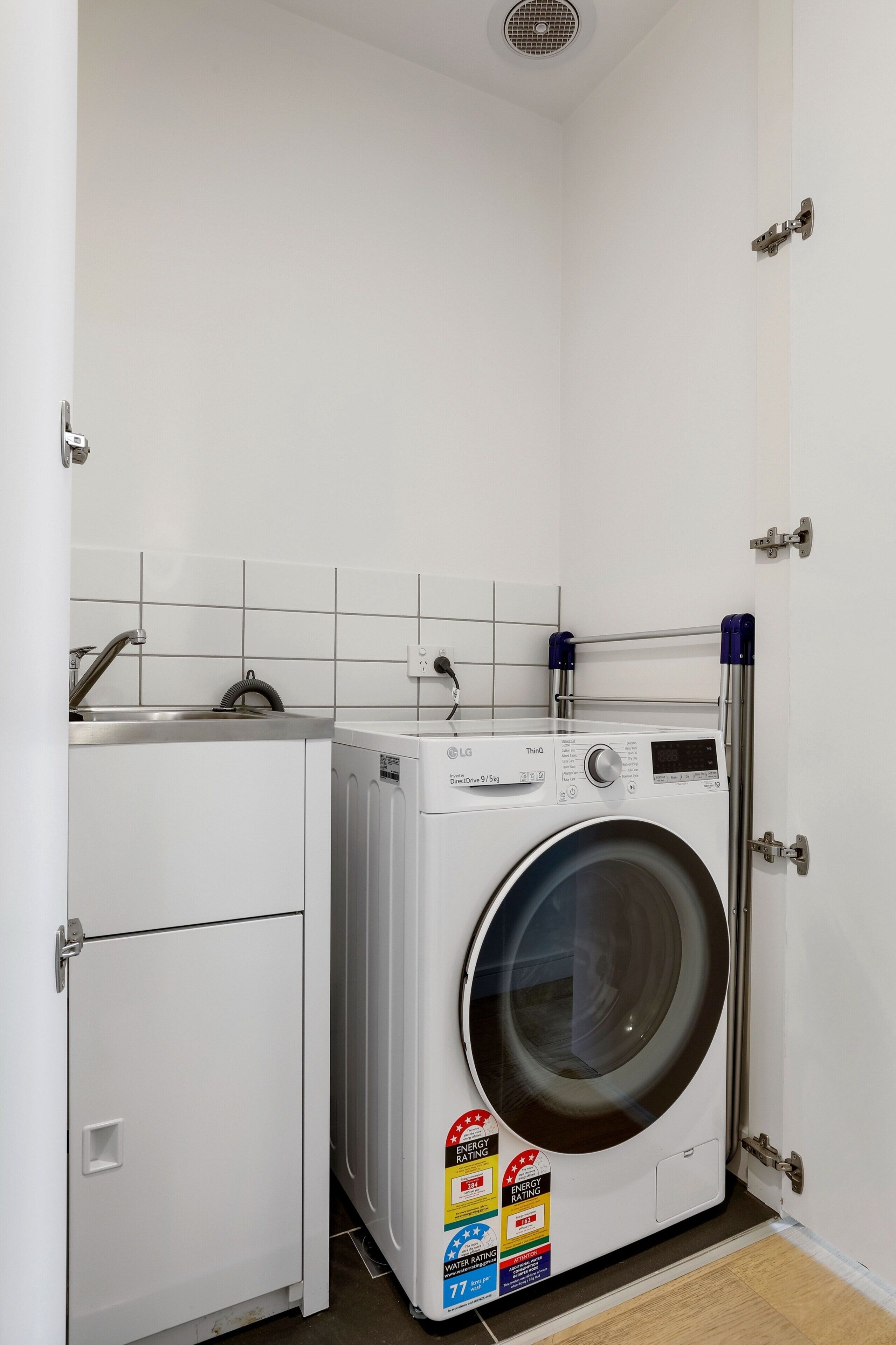 Een kleine wasruimte met een voorlader wasmachine, een klein kastje en een betegelde spatwand.