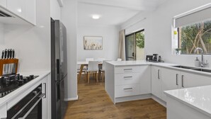 A modern kitchen with white cabinetry, a stainless steel refrigerator, and a wooden floor. - Coastal 3-bed House With BBQ and Private Courtyard (Adelaide)