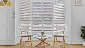A room with a bay window, two white chairs, a glass table, and a woven rug. - Coastal 3-bed House With BBQ and Private Courtyard (Adelaide)