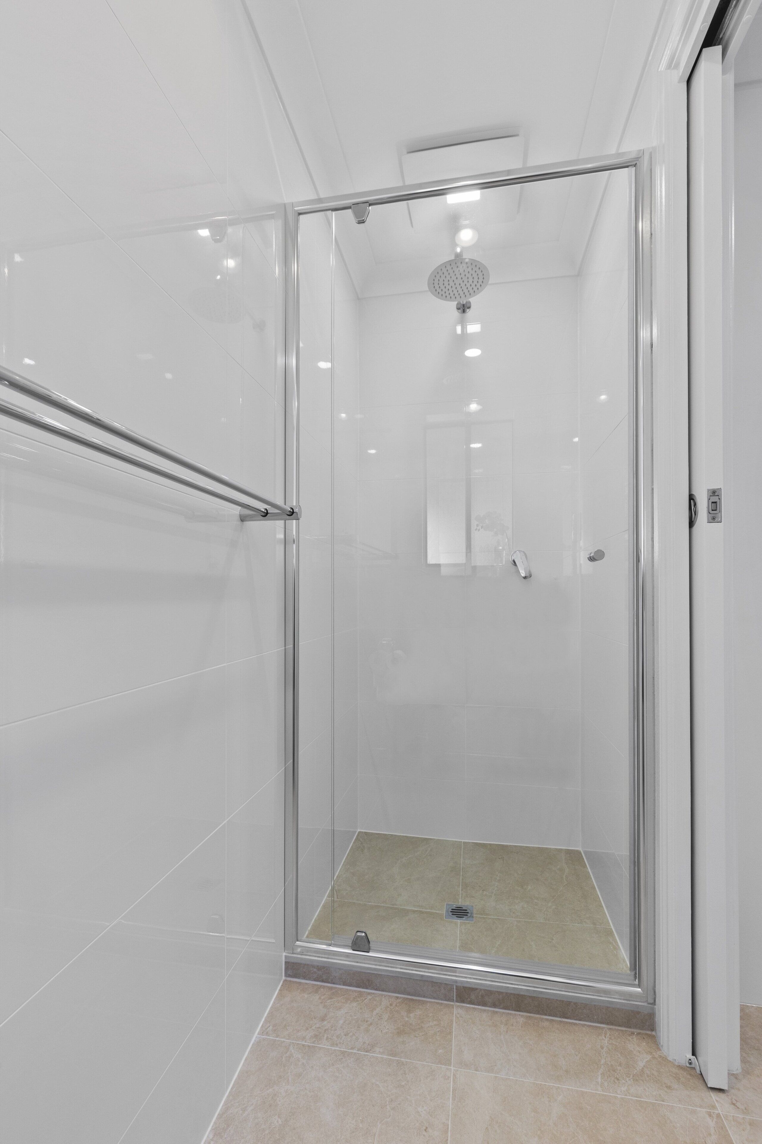Een moderne douche ruimte met een glazen deur, een metalen handgreep en een douchekop aan het plafond.