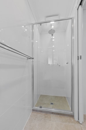 A modern shower area with a glass door, a metal handrail, and a ceiling-mounted showerhead. - Coastal 3-bed House With BBQ and Private Courtyard (Adelaide)