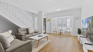 A modern living room with a staircase, grey sofas, a coffee table, and a dining area with chairs. - Coastal 3-bed House With BBQ and Private Courtyard (Adelaide)