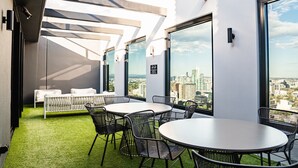 A modern rooftop lounge with round tables and chairs, a white sofa, and a view of the city skyline. - Stylish Southbank 1-bedroom With Pool and Gym (Melbourne)