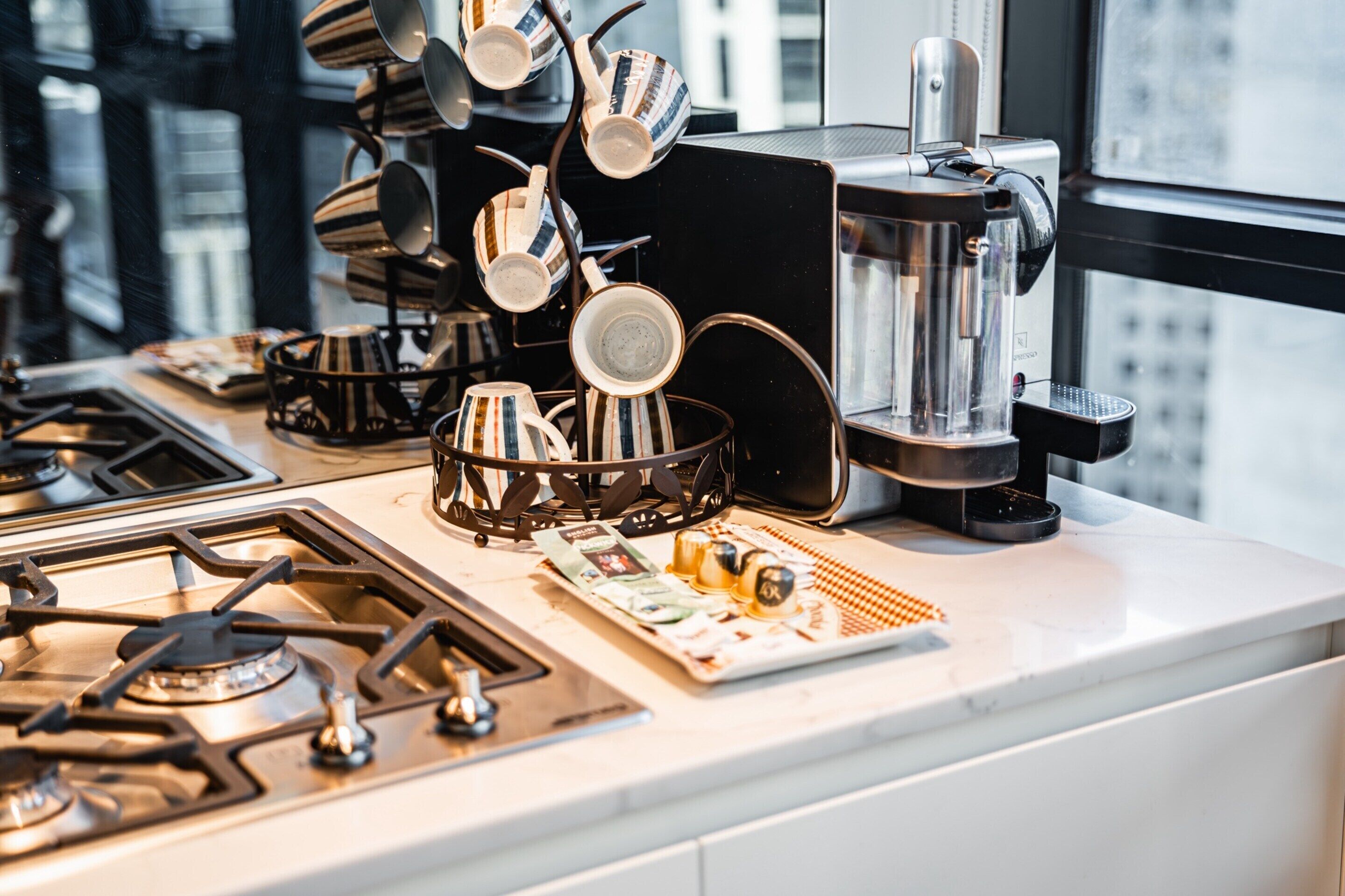 Una encimera de cocina con una cafetera, una estufa y un escurreplatos con varias tazas.