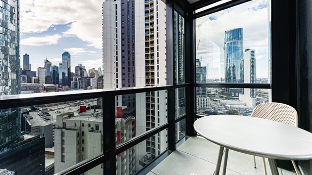 A high-rise apartment with a balcony, large windows, and a view of the city skyline. - Stylish Southbank 1-bedroom With Pool and Gym (Melbourne)