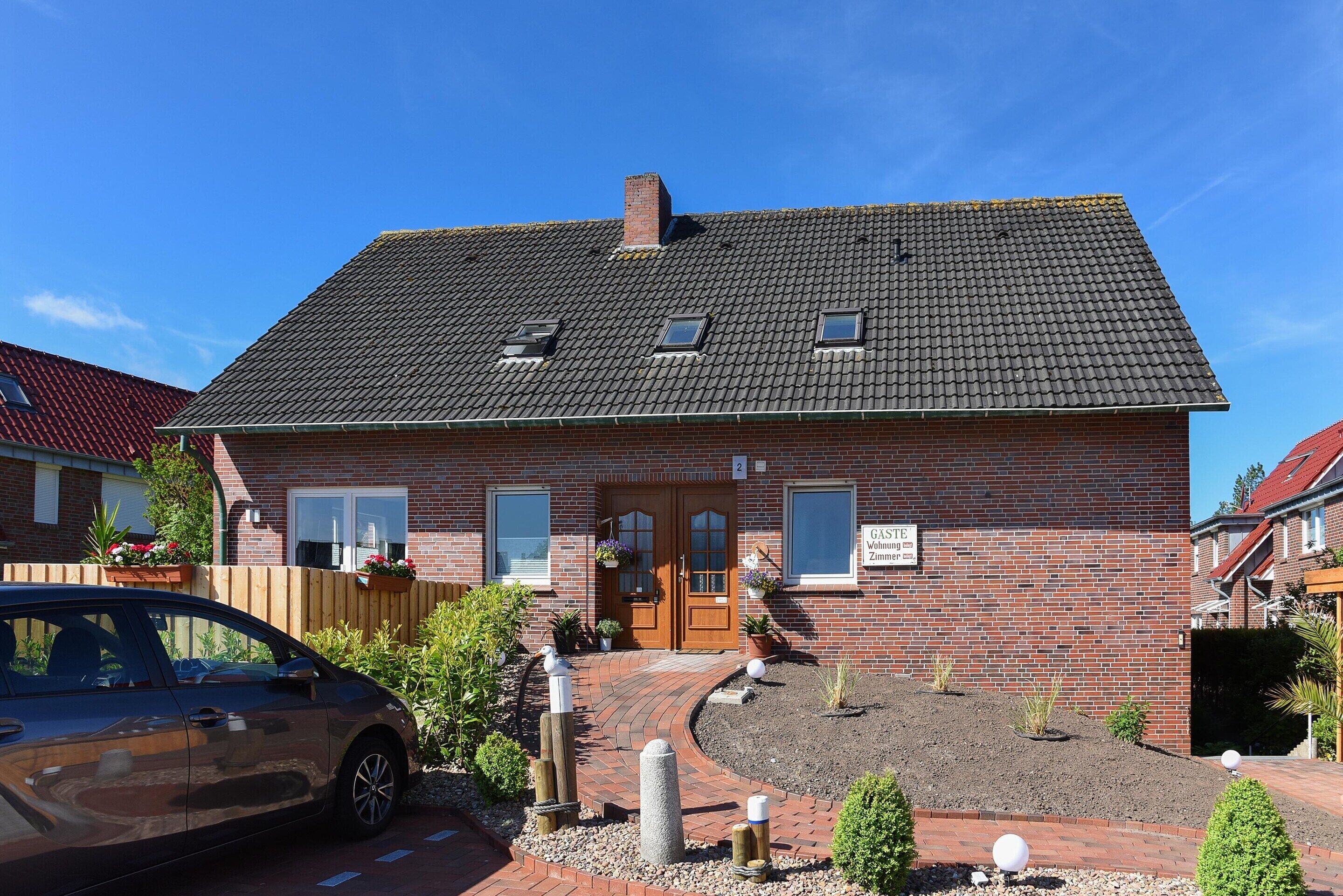 A two-story house with a brick facade, a tiled roof, and a small front garden with a pathway leading to the entrance.
