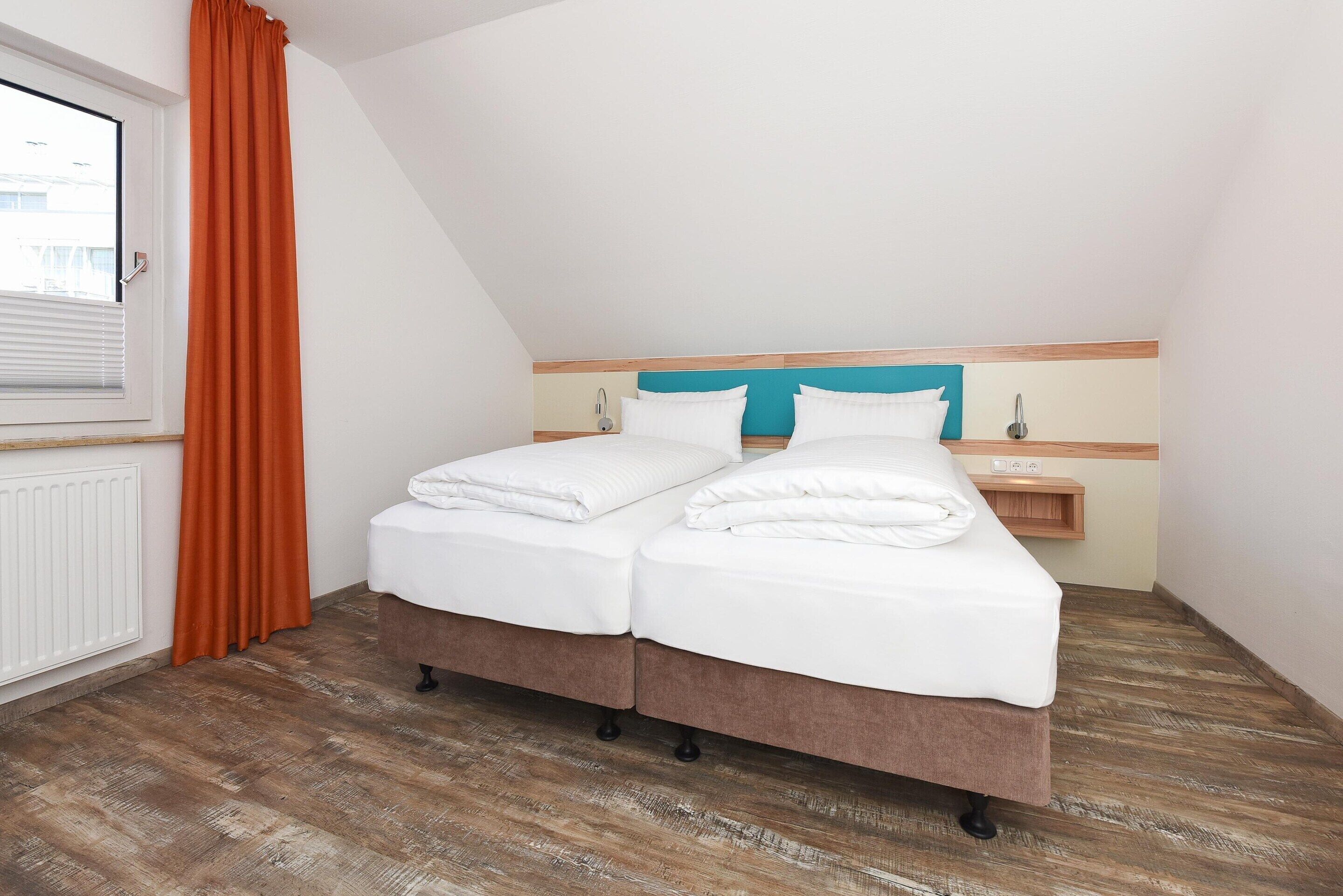 A bedroom with a bed, a window with blinds, a radiator, and a wooden floor.