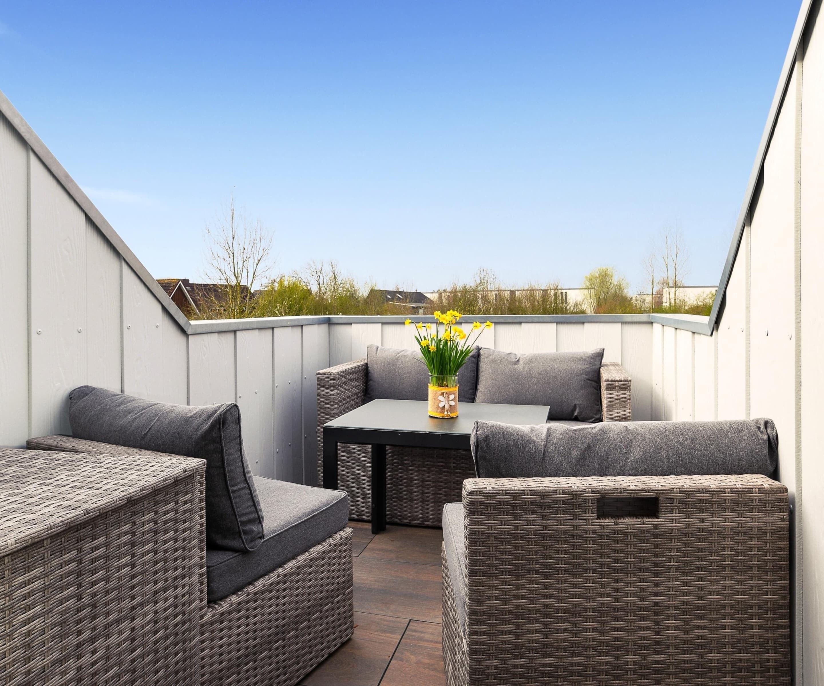 A rooftop patio with wicker furniture, a table, and a vase with flowers.