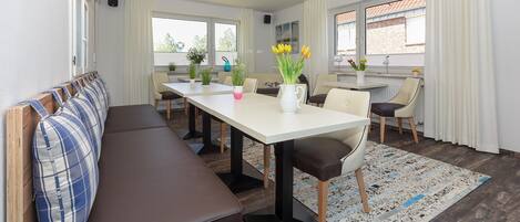 Un espace de salle à manger moderne avec une longue table, des chaises, un banc et un lustre.