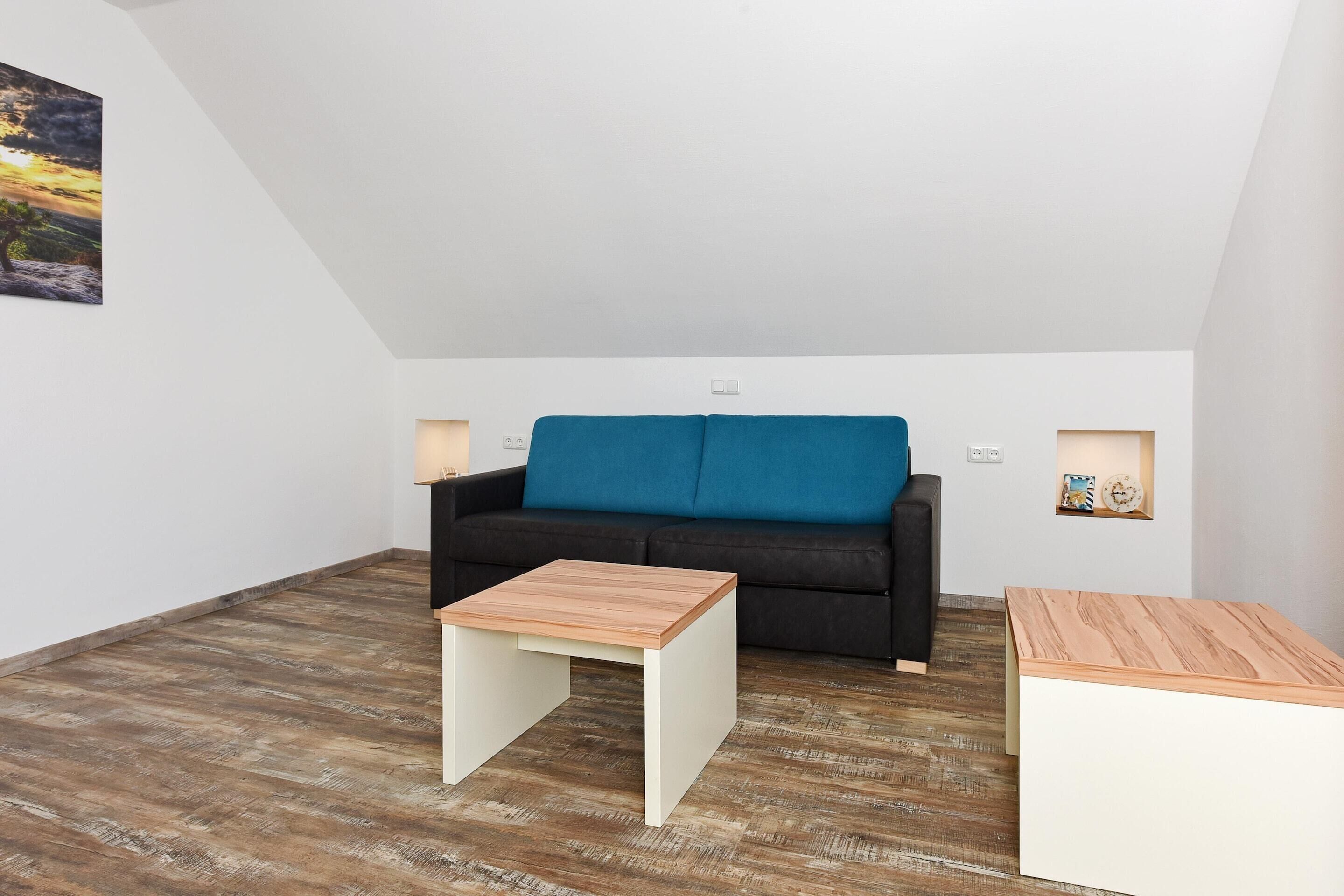 Un salon moderne avec un canapé noir, deux petites tables d’appoint blanches et une table basse en bois.