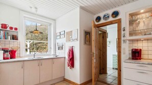 A kitchen with white cabinets, a window, and a door leading to another room. - 5 Star Holiday Home in Allinge (Allinge)