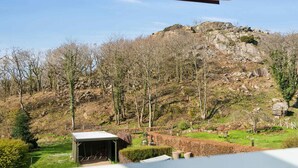 A view from a window overlooking a grassy area with a small shed and a rocky hill in the background. - 5 Star Holiday Home in Allinge (Allinge)