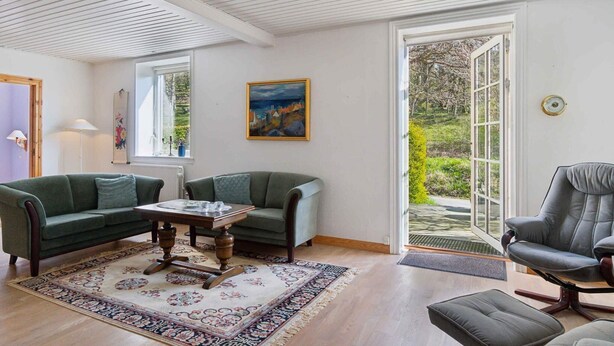 A spacious living room with two green sofas, a wooden coffee table, and a large window offering a view of greenery. - 5 Star Holiday Home in Allinge (Allinge)
