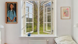 A bedroom with two beds, a window with open shutters, a radiator, and artwork on the walls. - 5 Star Holiday Home in Allinge (Allinge)