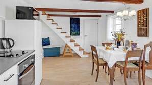 A compact kitchen with a built-in stove, a kettle, and a microwave. There is a dining area with a table set for two, surrounded by wooden chairs. A staircase with wooden steps leads to another room. - 4 Star Holiday Home in Norre Alslev (Norre Alslev)