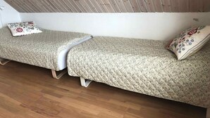 A small, cozy room with two single beds, each with a floral-patterned pillow. The room has a wooden sloped ceiling and a plain white wall. - 4 Star Holiday Home in Norre Alslev (Norre Alslev)