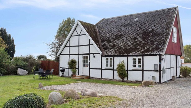 A traditional half-timbered house with a sloped roof, a gravel driveway, and a small garden with a table and chairs. - 4 Star Holiday Home in Norre Alslev (Norre Alslev)