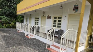 A building with a yellow facade, white railings, and multiple doors. - Prabhukrupa Tourist Farm (Alibag)