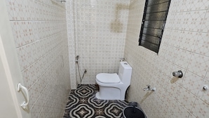 A small bathroom with a toilet, a shower, and a sink. The floor has a geometric patterned tile design. - Prabhukrupa Tourist Farm (Alibag)