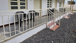 A building with a covered outdoor seating area, a staircase, and a number '003' sign. - Prabhukrupa Tourist Farm (Alibag)