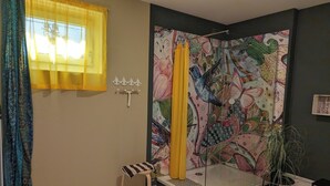 Une douche agrémentée d’une fresque murale colorée, un petit tabouret et une cabine de douche en verre.