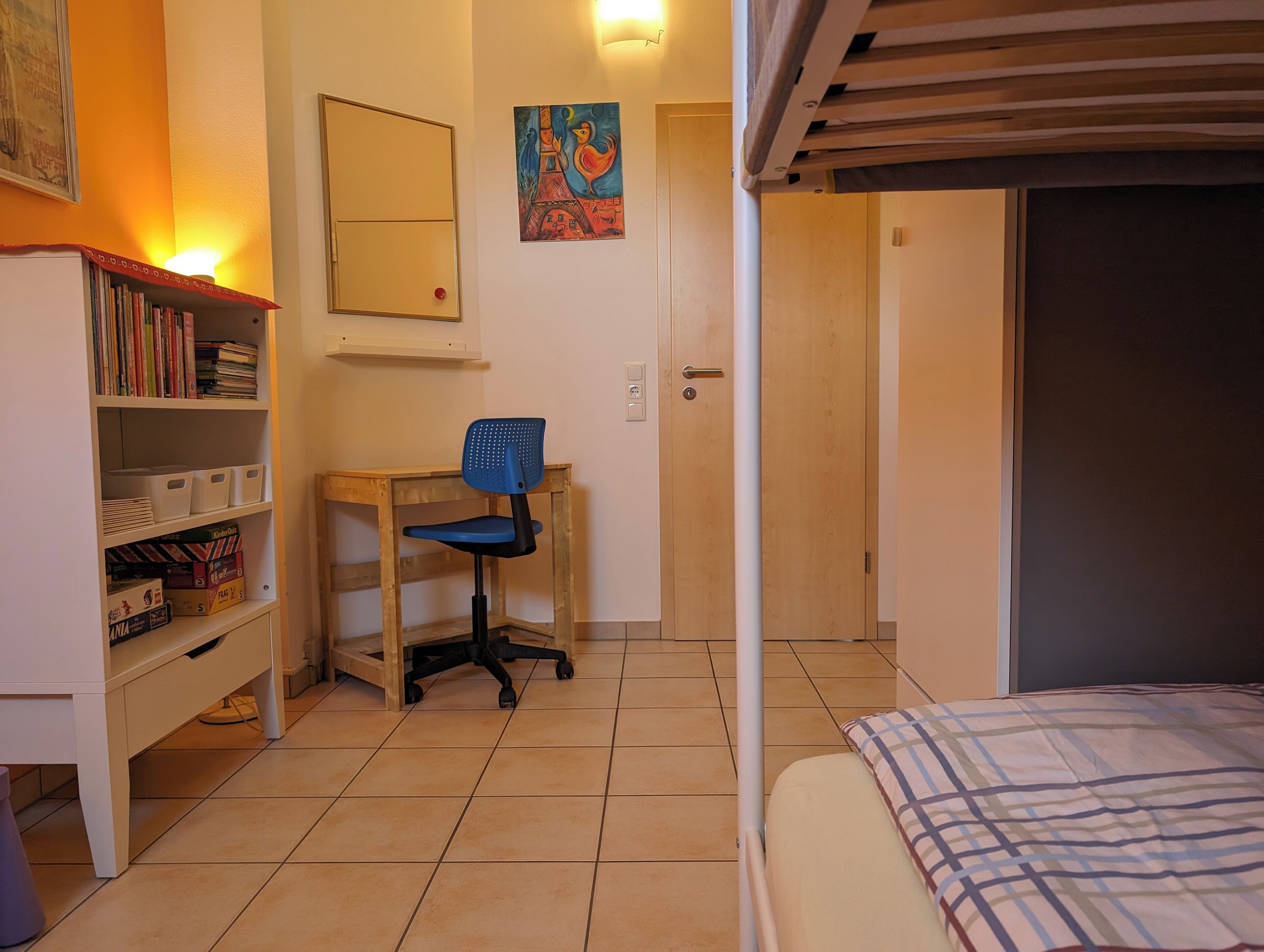 A bedroom with a bed, a desk with a chair, a bookshelf, and a door leading to another room.