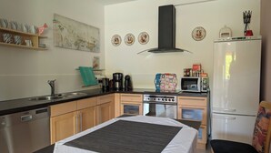 Une cuisine compacte équipée d’un lave-vaisselle, d’une cuisinière, d’un four à micro-ondes et d’un réfrigérateur. On y trouve un lit avec une couverture blanche et un oreiller noir.