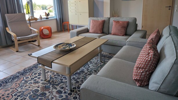 Un salon comprenant un canapé, un fauteuil et une table basse. Il y a une fenêtre avec des rideaux, un meuble et des œuvres d’art accrochées aux murs.