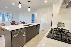 Una cucina moderna con lavastoviglie, piano cottura a gas, luci a sospensione e un'area pranzo con sedie.