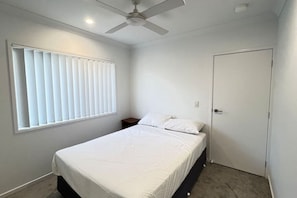 Un dormitorio con cama, ventilador de techo, ventana con persianas y puerta.